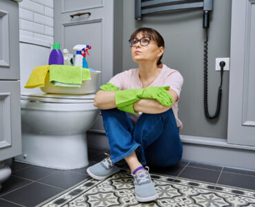 Tired woman sitting on the floor after cleaning bathroom, toilet. Routine house cleaning, home hygiene, housecleaning service, housekeeping, housework